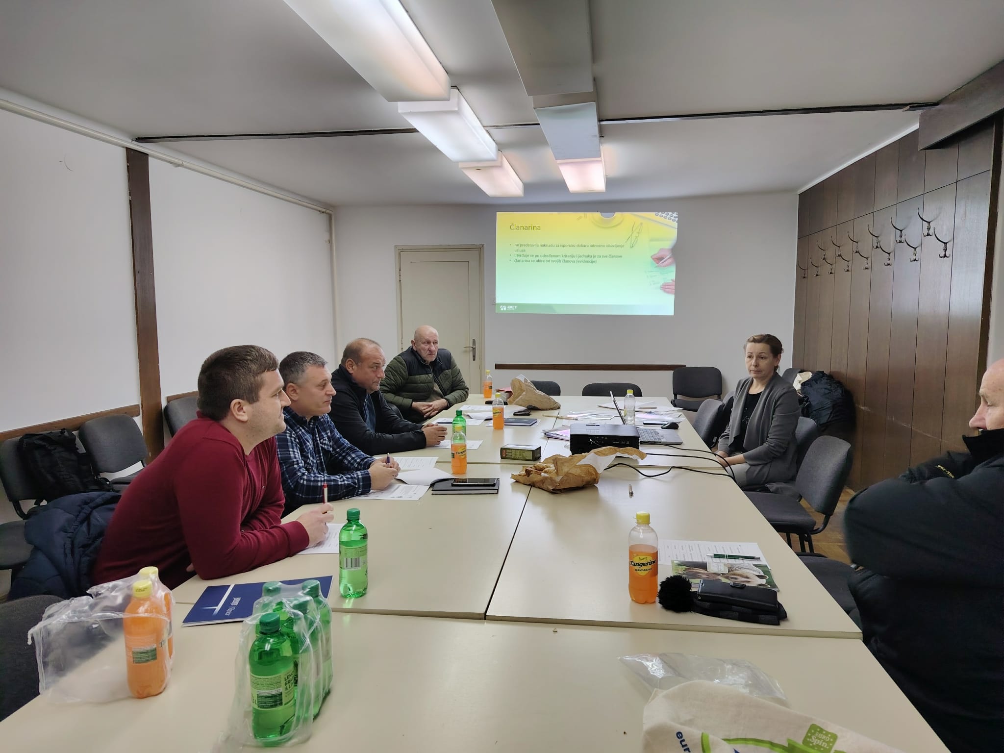 Sudionici radionice sjede za stolom i prate prezentaciju o članarini u konferencijskoj dvorani.